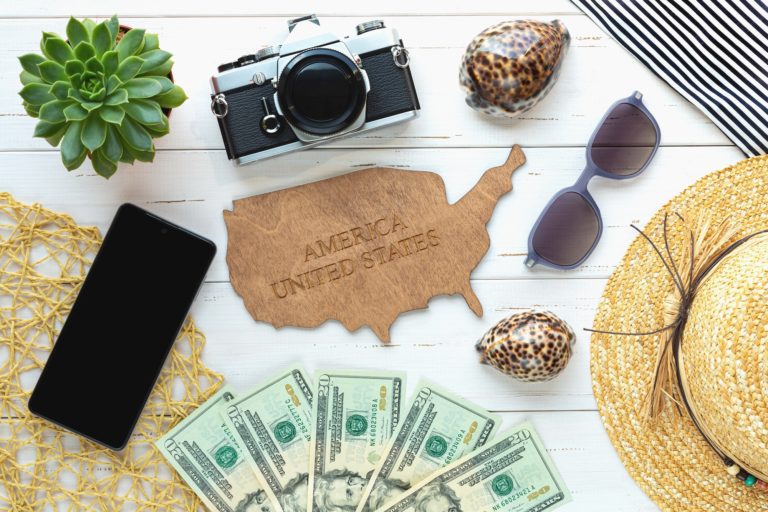 On a white background, a wooden map of the USA, travel accessories, money.